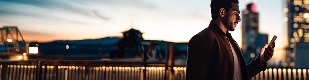 Man looking down at mobile phone at sunset